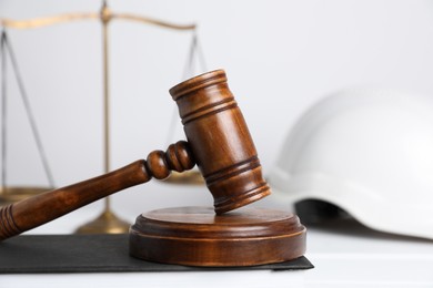 Photo of Accident at work concept. Gavel, scales and construction worker's protective gear on white wooden table, selective focus