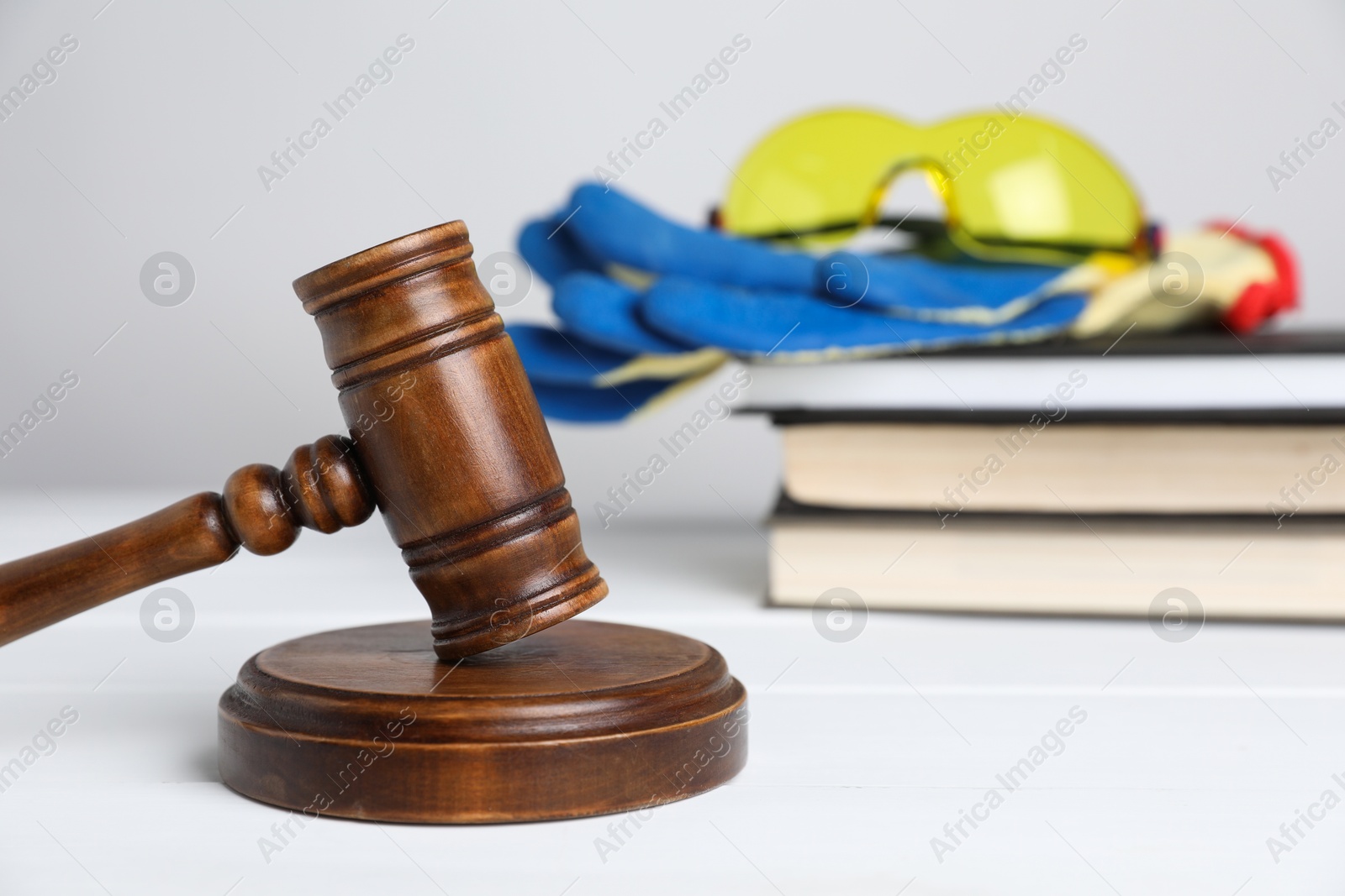 Photo of Accident at work concept. Gavel, books and construction worker's protective gear on white wooden table, selective focus