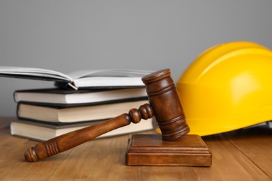 Photo of Accident at work concept. Gavel, books and construction worker's protective gear on wooden table, selective focus