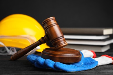 Photo of Accident at work concept. Gavel, books and construction worker's protective gear on black wooden table, selective focus