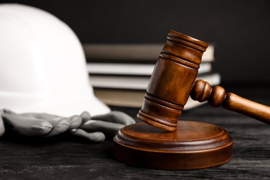 Photo of Accident at work concept. Gavel, books and construction worker's protective gear on black wooden table, selective focus