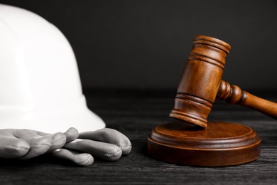 Photo of Accident at work concept. Gavel and construction worker's protective gear on black wooden table