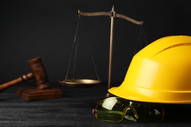 Photo of Accident at work concept. Gavel, scales and construction worker's protective gear on black wooden table, selective focus