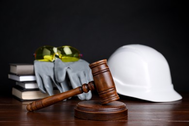 Photo of Accident at work concept. Gavel, books and construction worker's protective gear on wooden table, selective focus