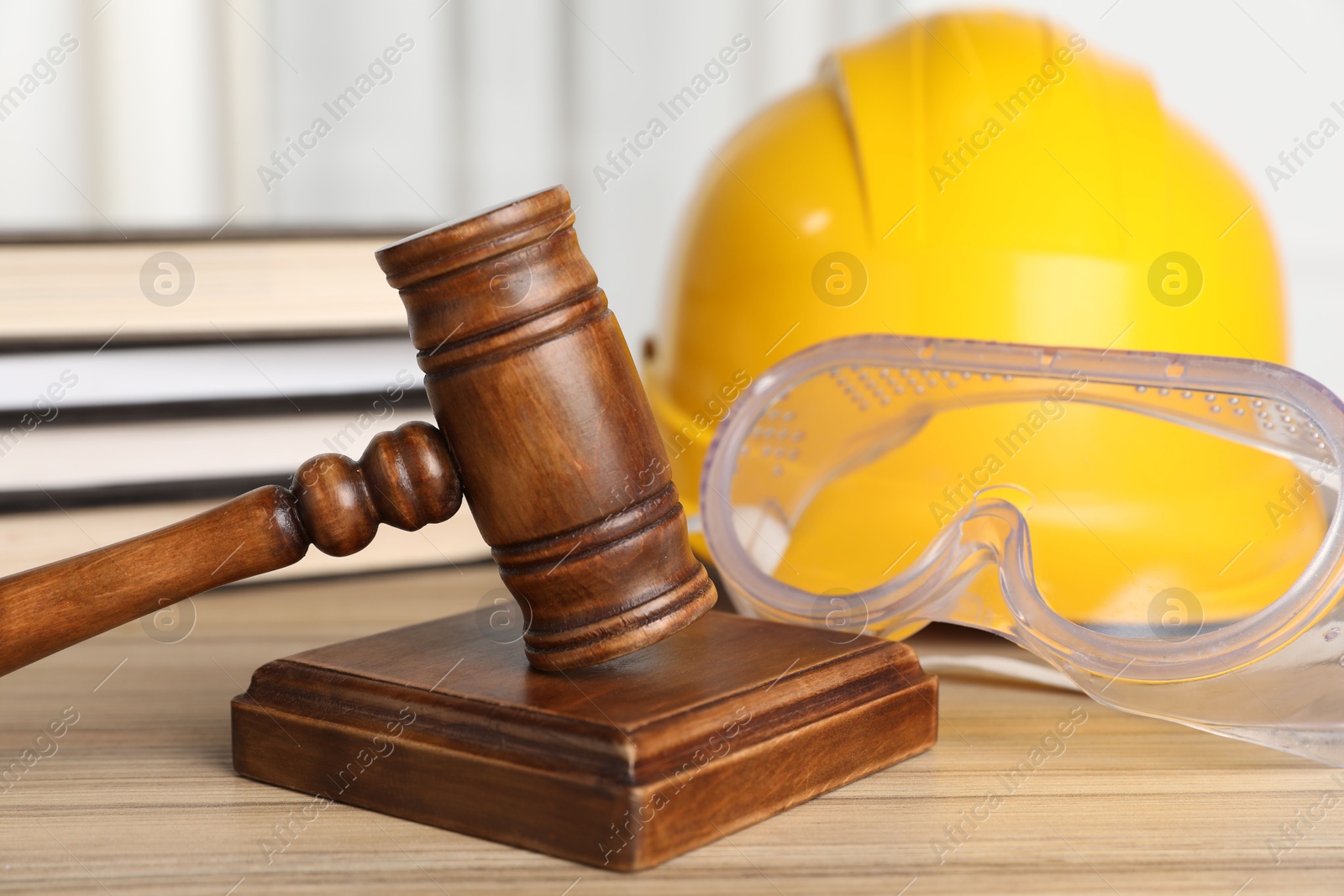 Photo of Accident at work. Gavel, goggles, hardhat and stack of books on wooden table, closeup