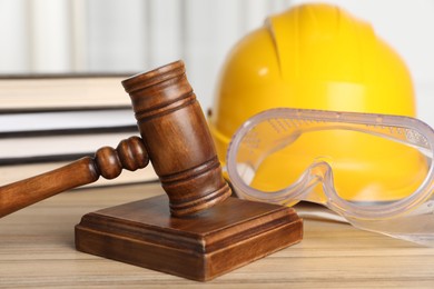 Photo of Accident at work. Gavel, goggles, hardhat and stack of books on wooden table, closeup