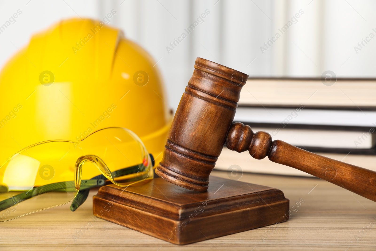 Photo of Accident at work. Gavel, goggles, hardhat and stack of books on wooden table, closeup