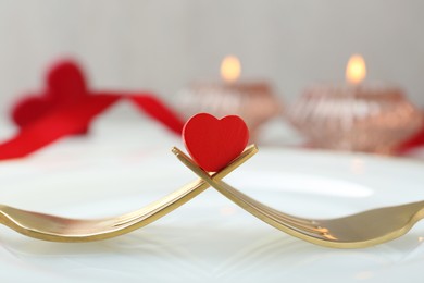 Photo of Romantic table setting for Valentine's day. Decorative heart between forks on white plate, closeup