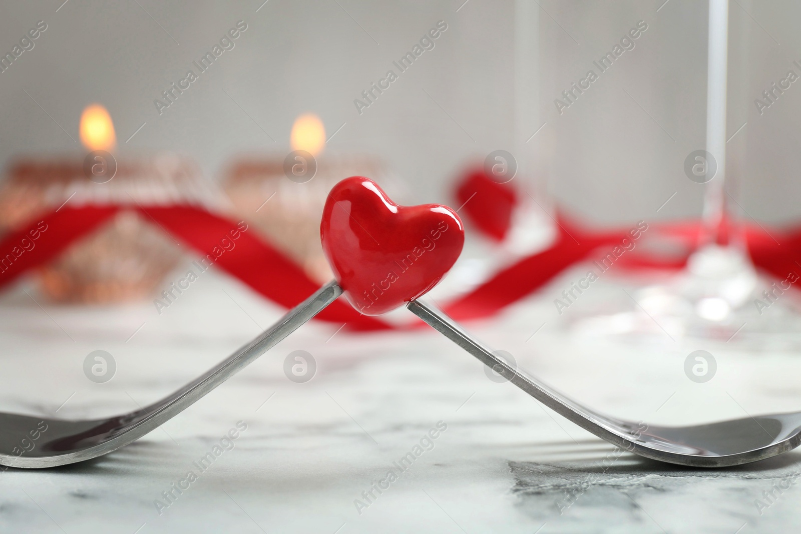 Photo of Romantic place setting for Valentine's day. Decorative heart between forks on white marble table, closeup