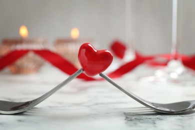 Romantic place setting for Valentine's day. Decorative heart between forks on white marble table, closeup