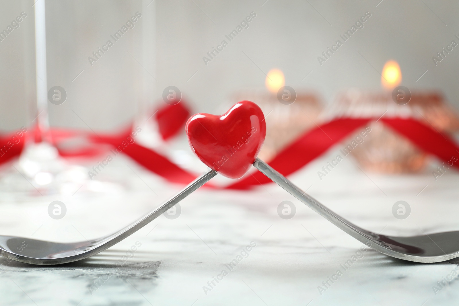 Photo of Romantic place setting for Valentine's day. Decorative heart between forks on white marble table, closeup