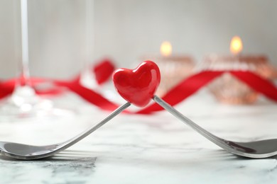 Photo of Romantic place setting for Valentine's day. Decorative heart between forks on white marble table, closeup