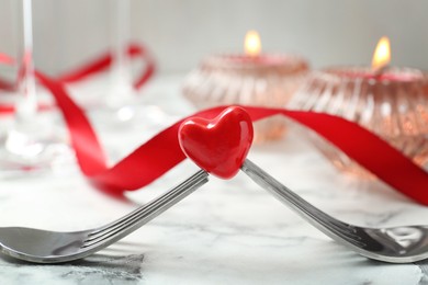 Photo of Romantic place setting for Valentine's day. Decorative heart between forks on white marble table, closeup