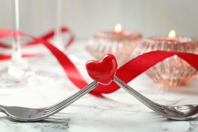 Photo of Romantic place setting for Valentine's day. Decorative heart between forks on white marble table, closeup