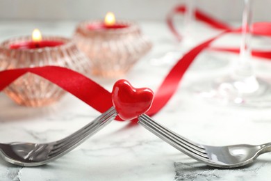 Photo of Romantic place setting for Valentine's day. Decorative heart between forks on white marble table, closeup