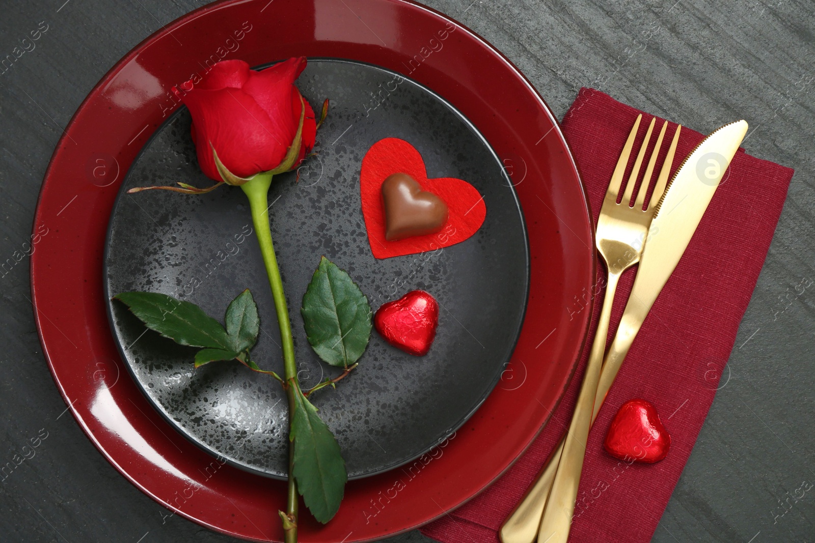 Photo of Romantic place setting with rose and plates on black table, top view. Valentine's day celebration