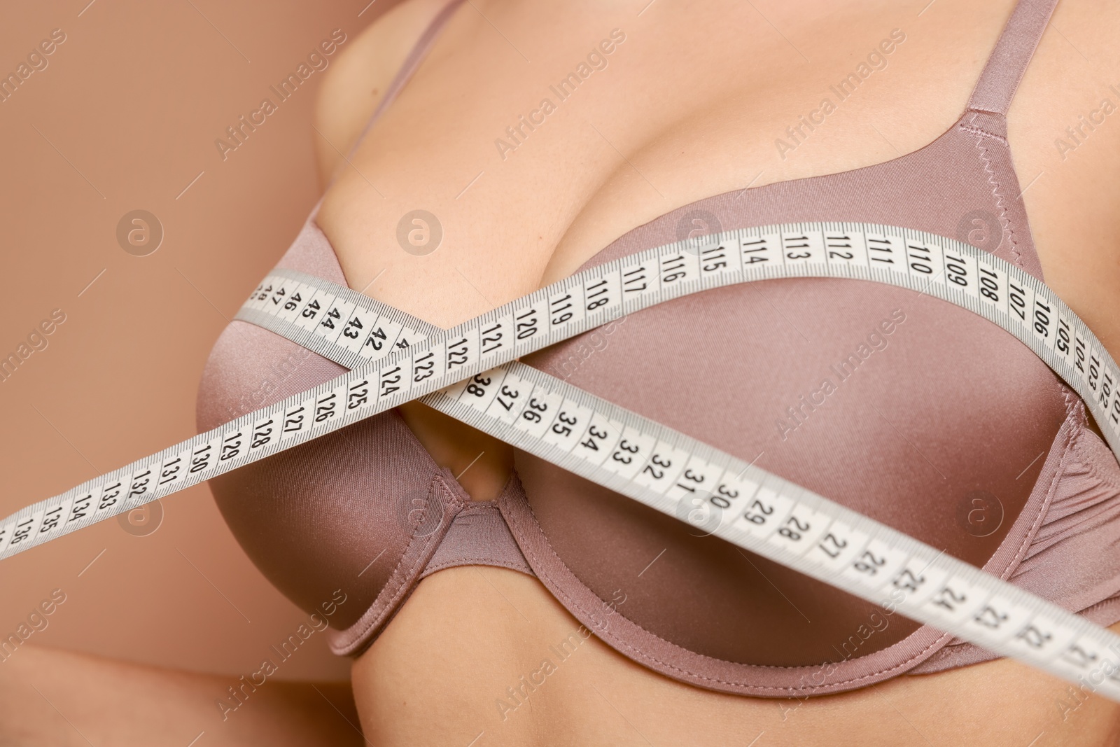 Photo of Woman in beautiful bra measuring breast circumference on beige background, closeup