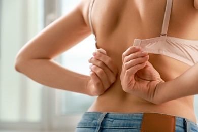 Photo of Woman putting on comfortable bra indoors, closeup