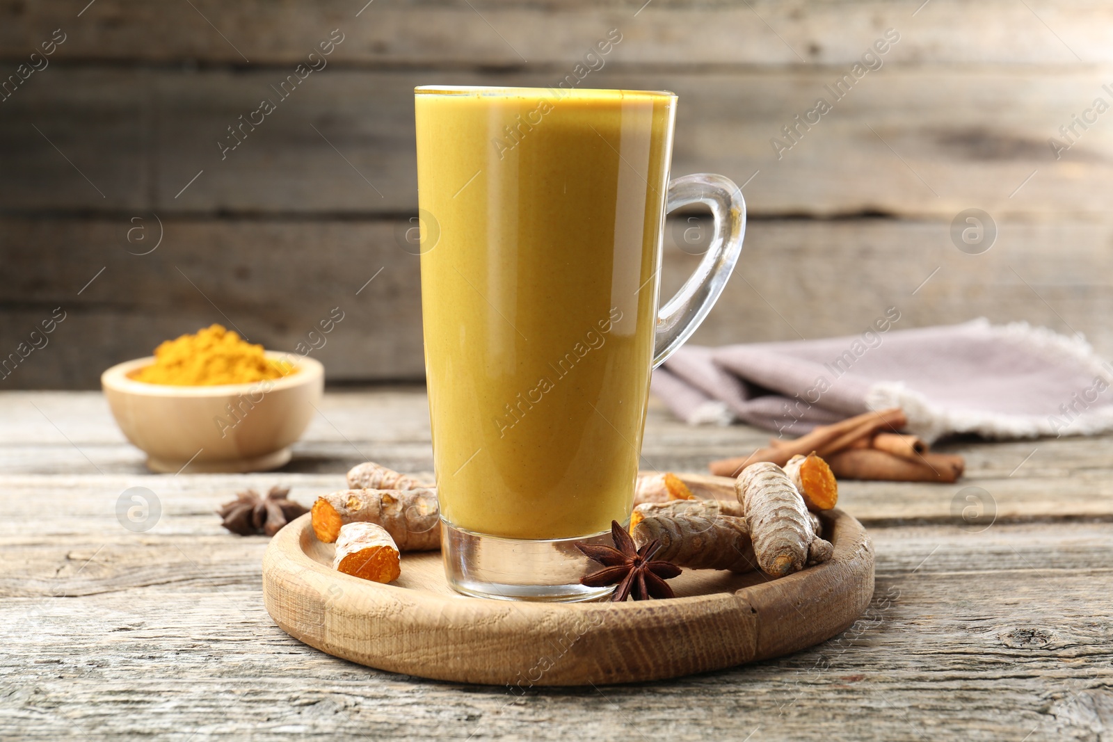 Photo of Delicious turmeric latte in glass cup, roots and spices on wooden table, closeup