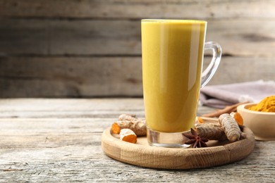 Photo of Delicious turmeric latte in glass cup, roots and spices on wooden table, closeup. Space for text