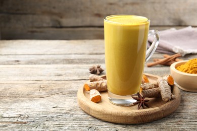 Photo of Delicious turmeric latte in glass cup, roots and spices on wooden table, closeup. Space for text