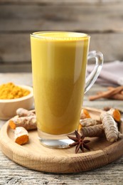 Photo of Delicious turmeric latte in glass cup, roots and anise star on wooden table, closeup