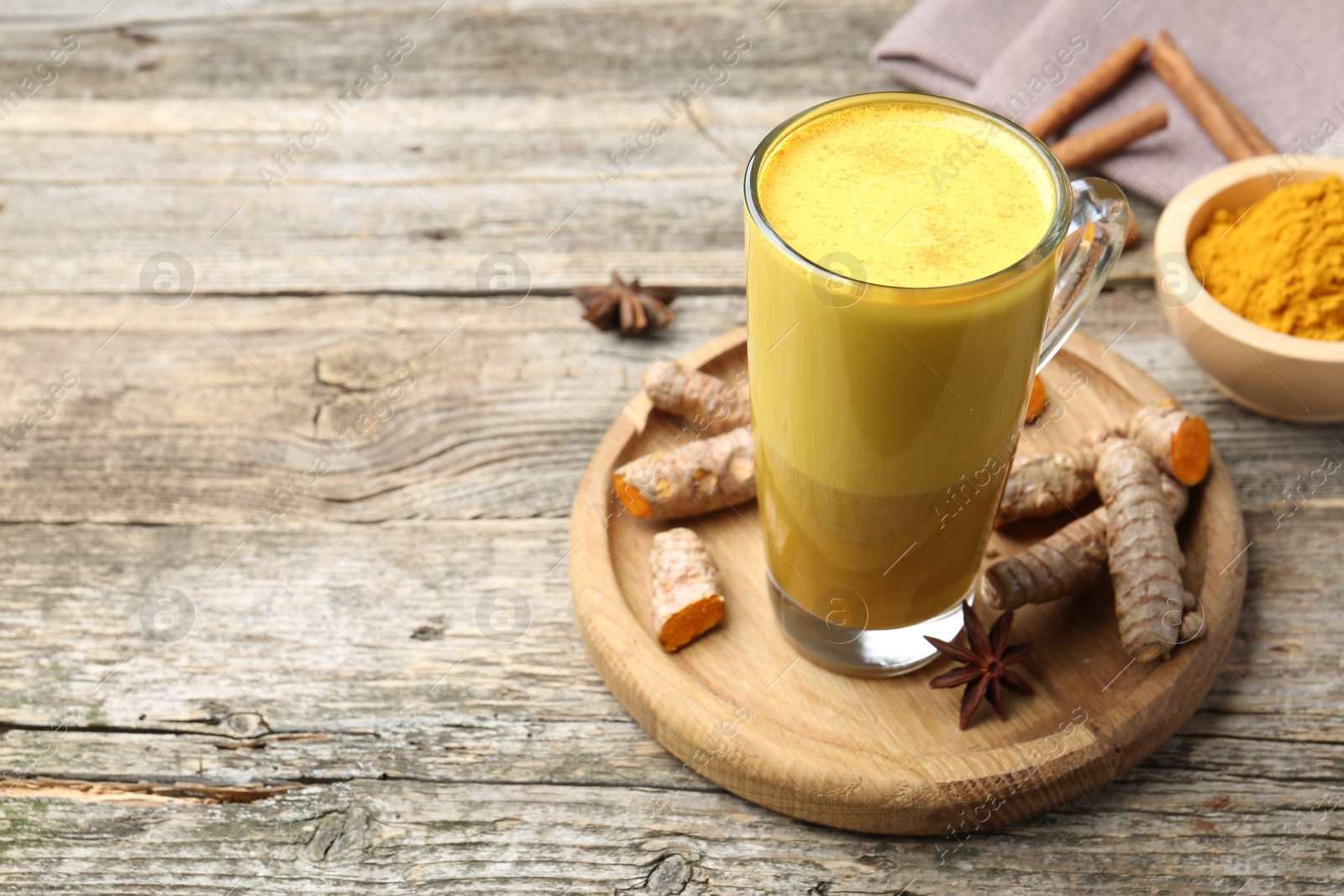 Photo of Delicious turmeric latte in glass cup, roots and spices on wooden table. Space for text