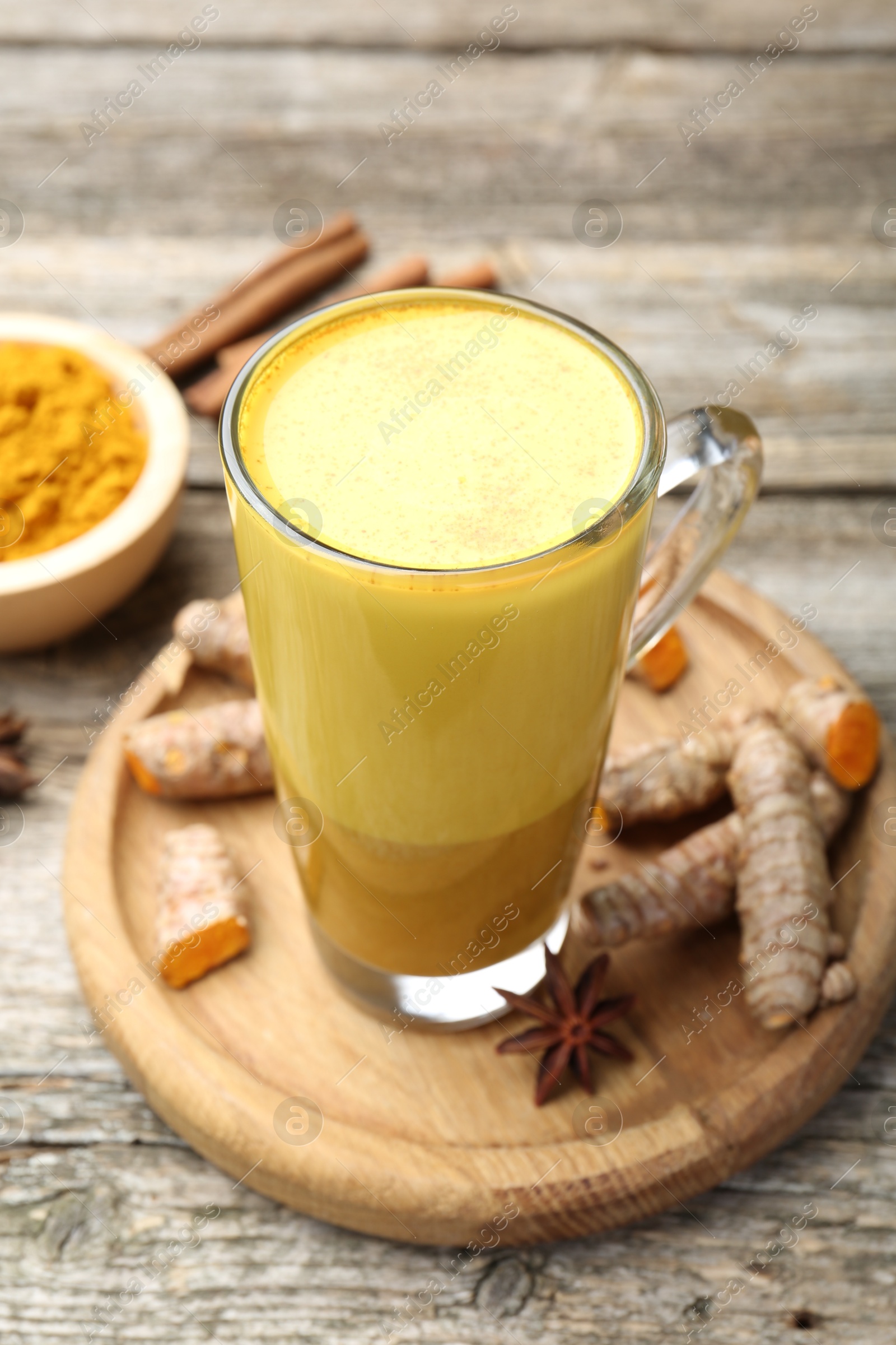 Photo of Delicious turmeric latte in glass cup, roots and spices on wooden table, closeup