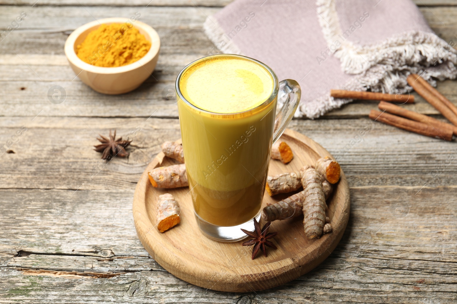 Photo of Delicious turmeric latte in glass cup, roots and spices on wooden table