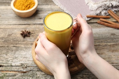 Photo of Woman with glass cup of delicious turmeric latte at wooden table, closeup