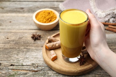 Photo of Woman with glass cup of delicious turmeric latte at wooden table, closeup