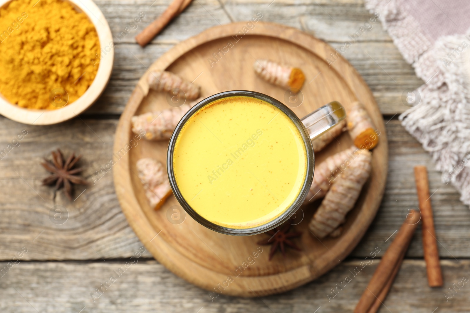 Photo of Delicious turmeric latte in glass cup, roots and spices on wooden table, flat lay