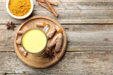 Photo of Delicious turmeric latte in glass cup, roots and spices on wooden table, flat lay. Space for text