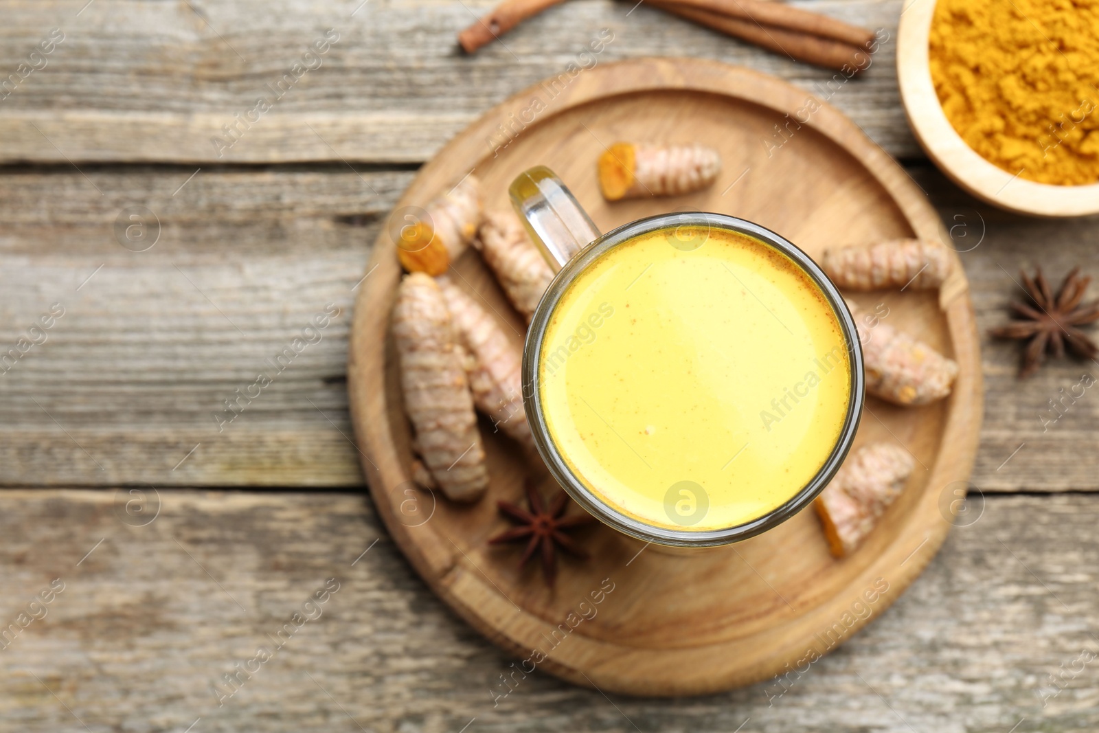 Photo of Delicious turmeric latte in glass cup, roots and spices on wooden table, flat lay