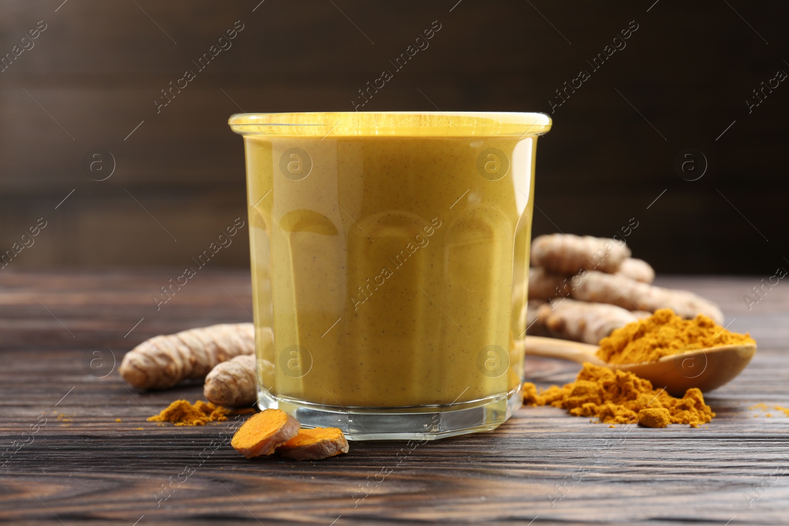 Photo of Delicious turmeric latte in glass, roots and powder on wooden table, closeup