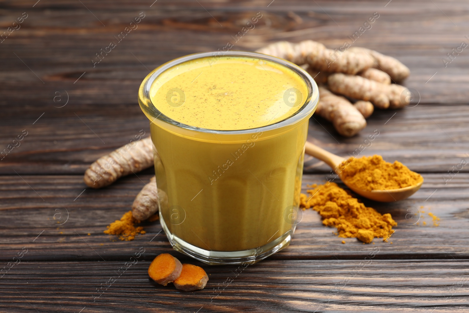 Photo of Delicious turmeric latte in glass, roots and powder on wooden table, closeup