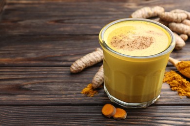 Photo of Delicious turmeric latte in glass, roots and powder on wooden table, closeup. Space for text