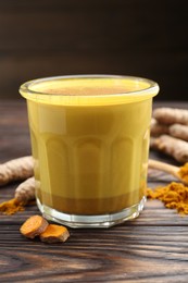 Photo of Delicious turmeric latte in glass, roots and powder on wooden table, closeup