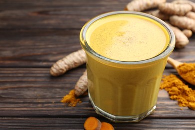 Photo of Delicious turmeric latte in glass, roots and powder on wooden table, closeup