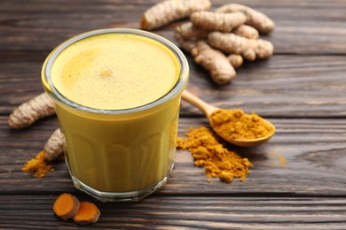 Photo of Delicious turmeric latte in glass, roots and powder on wooden table, closeup. Space for text