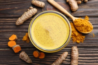 Photo of Delicious turmeric latte in glass, roots and powder on wooden table, top view