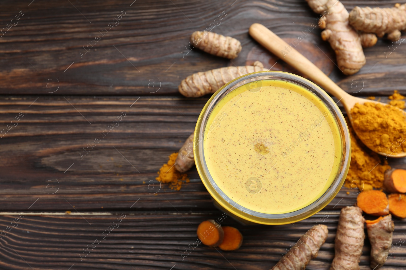 Photo of Delicious turmeric latte in glass, roots and powder on wooden table, top view. Space for text