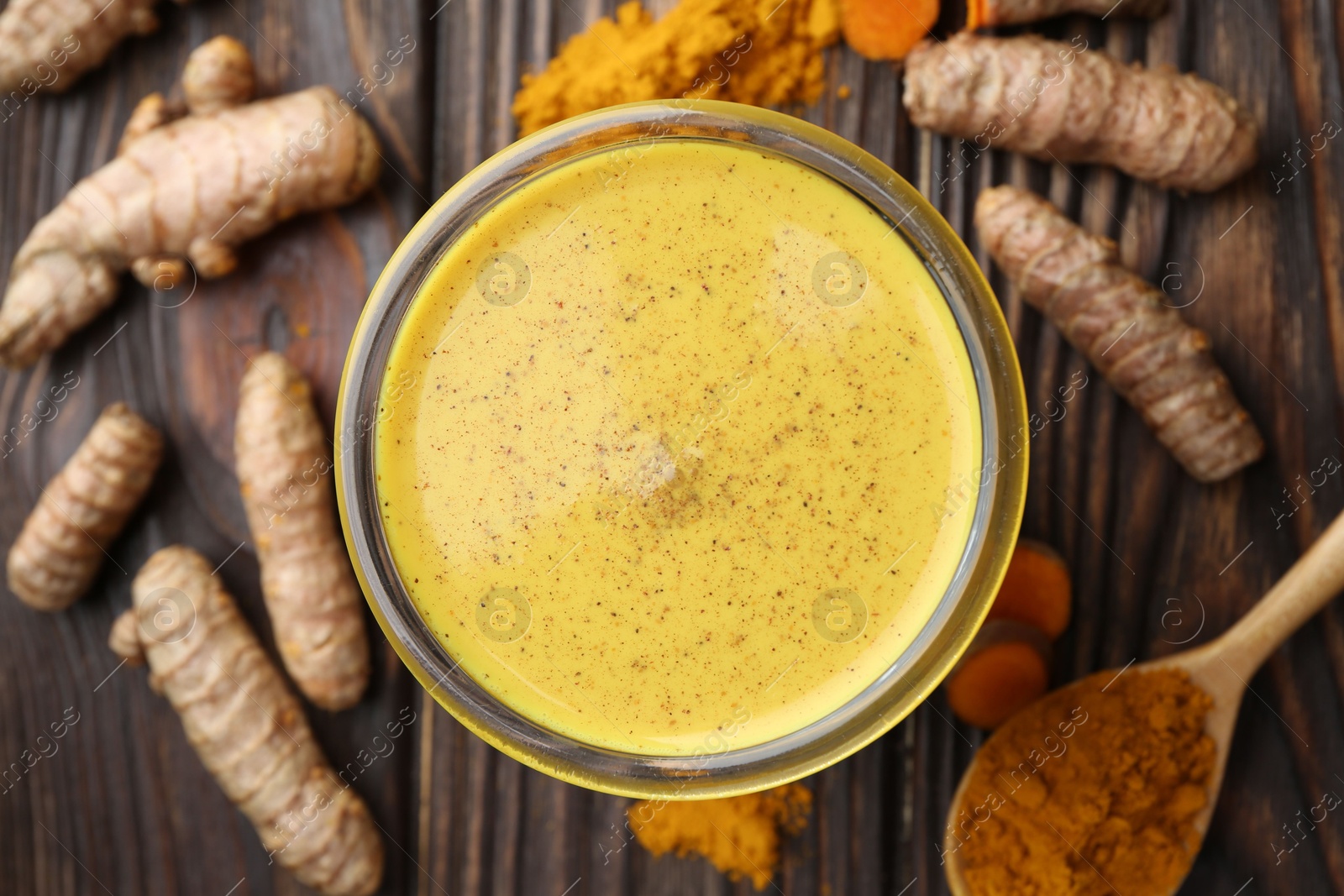 Photo of Delicious turmeric latte in glass, roots and powder on wooden table, top view