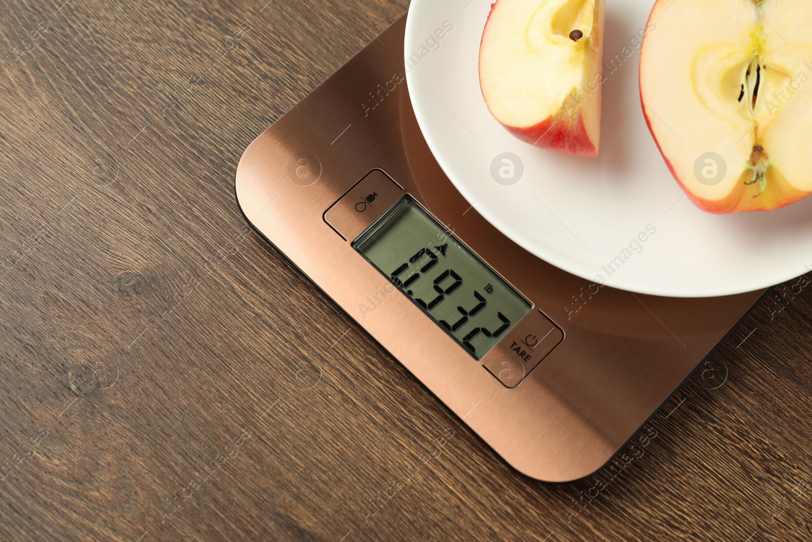 Photo of Modern electronic kitchen scale with cut apple on wooden table, closeup. Space for text