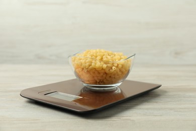 Photo of Modern electronic kitchen scale with bowl of raw pasta on wooden table, closeup