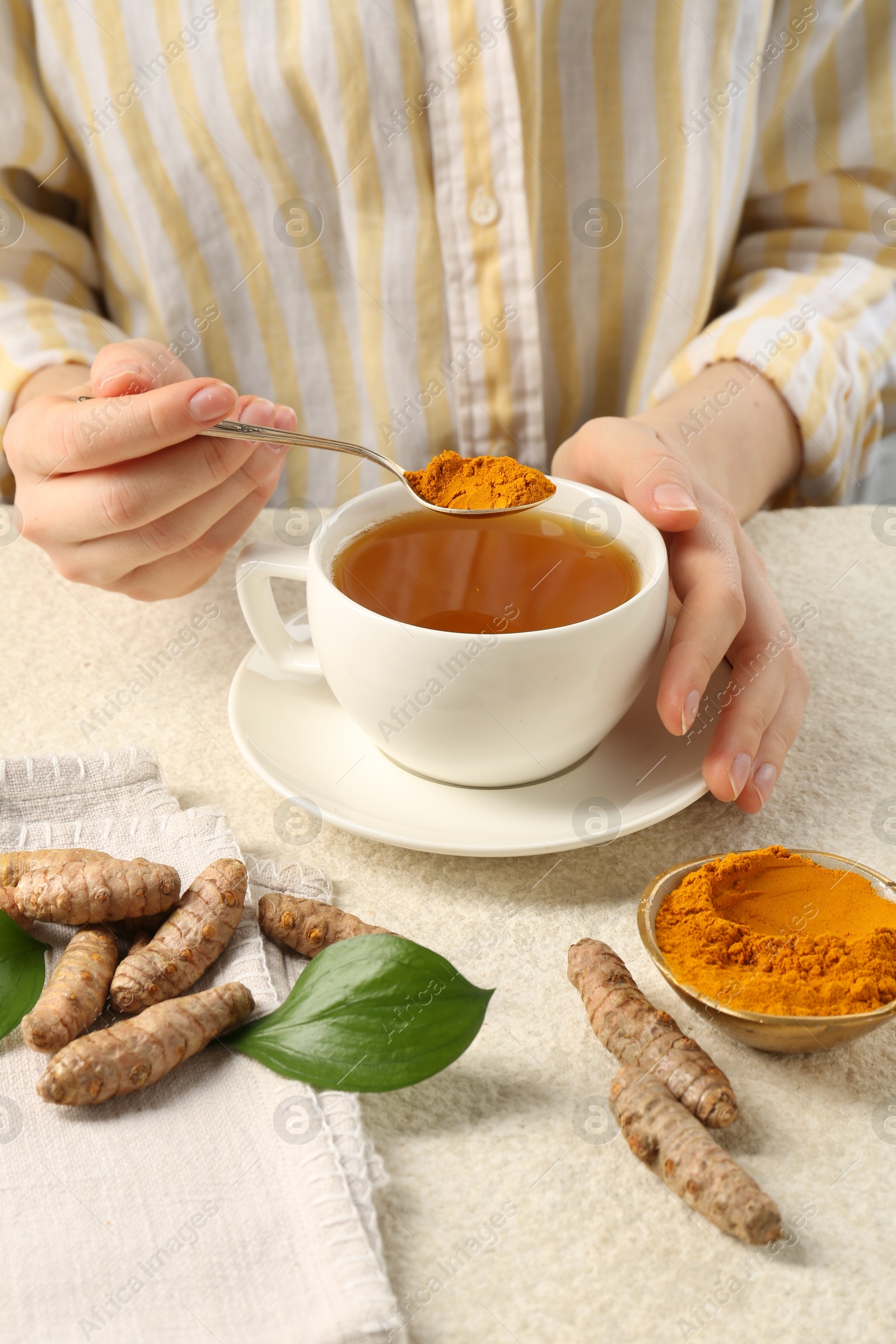 Photo of Woman making turmeric tea at white textured table, closeup