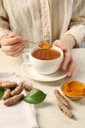 Photo of Woman making turmeric tea at white textured table, closeup