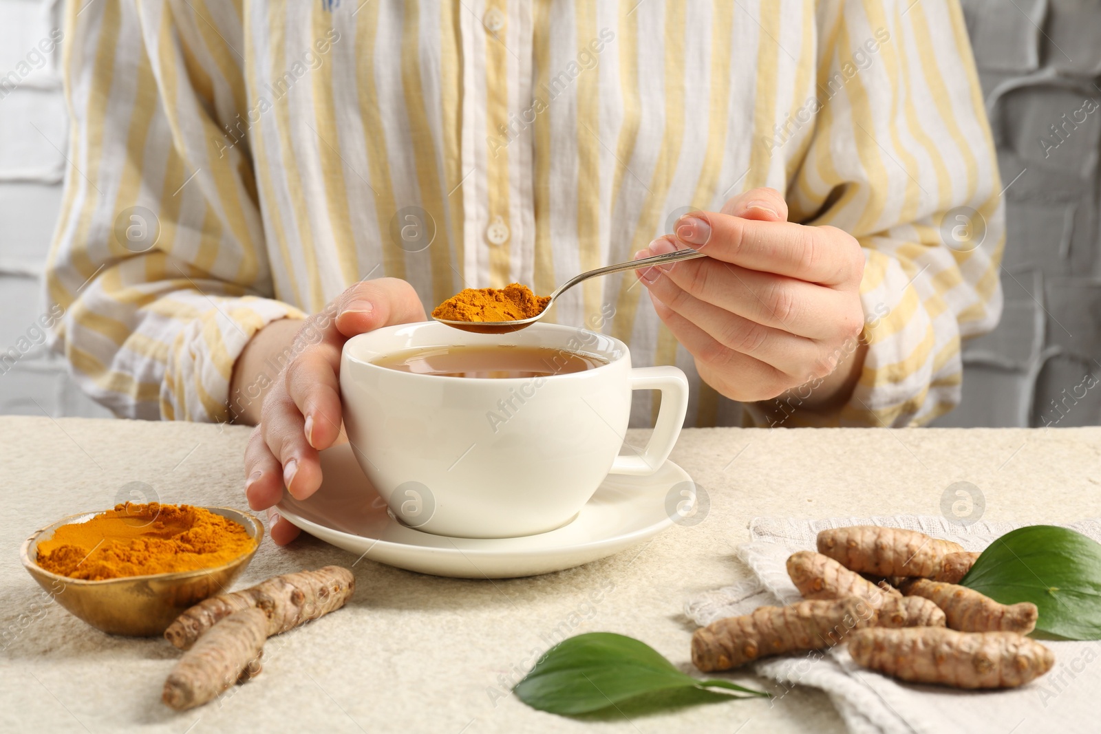 Photo of Woman making turmeric tea at white textured table, closeup