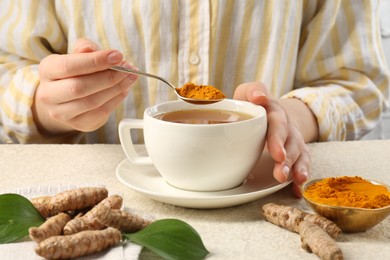 Photo of Woman making turmeric tea at white textured table, closeup