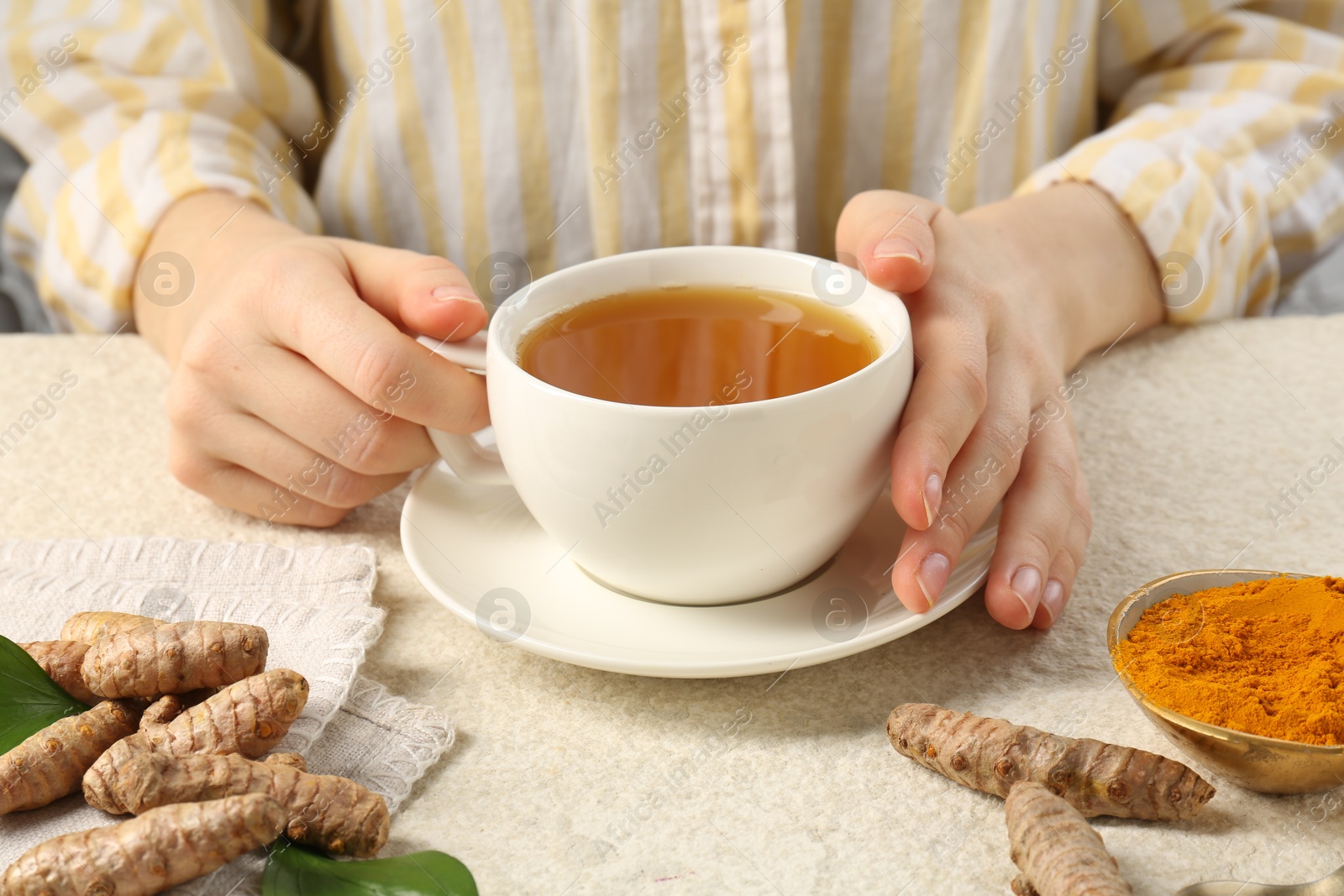 Photo of Woman drinking turmeric tea at white textured table, closeup